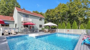 A swimming pool with a wooden deck, lounge chairs, and umbrellas. - 3-bedroom house in Jamesport with pool (Jamesport)