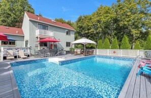 A swimming pool with a wooden deck, lounge chairs, and umbrellas. - 3-bedroom house in Jamesport with pool (Jamesport)