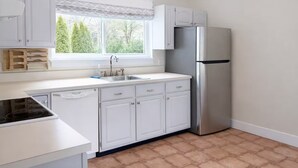A kitchen with white cabinets, a stainless steel refrigerator, a window with a view of trees, and a tiled floor. - 3-bedroom house in Jamesport with pool (Jamesport)