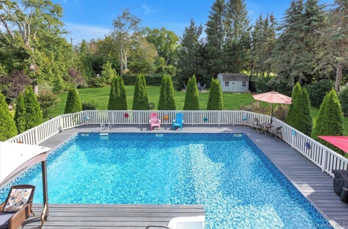 Une piscine rectangulaire dotée d’une terrasse en bois et d’une rambarde blanche.