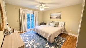 A bedroom with a bed, a nightstand, a ceiling fan, a window with curtains, and a painting on the wall. - 3-bedroom house in Jamesport with pool (Jamesport)
