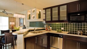 Una cucina moderna con mobili in legno scuro, lavastoviglie in acciaio inossidabile e una parete di fondo rivestita di piastrelle verdi.