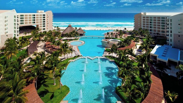 Un resort con una grande piscina centrale, palme e vista sull'oceano.