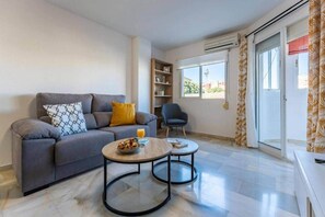 Ein Wohnzimmer mit einer Couch, zwei Couchtischen, einem Sessel und einem Bücherregal.