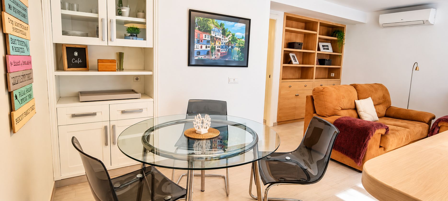 Uma sala de estar moderna com uma mesa de jantar de vidro, cadeiras pretas, um sofá marrom e uma estante de madeira.