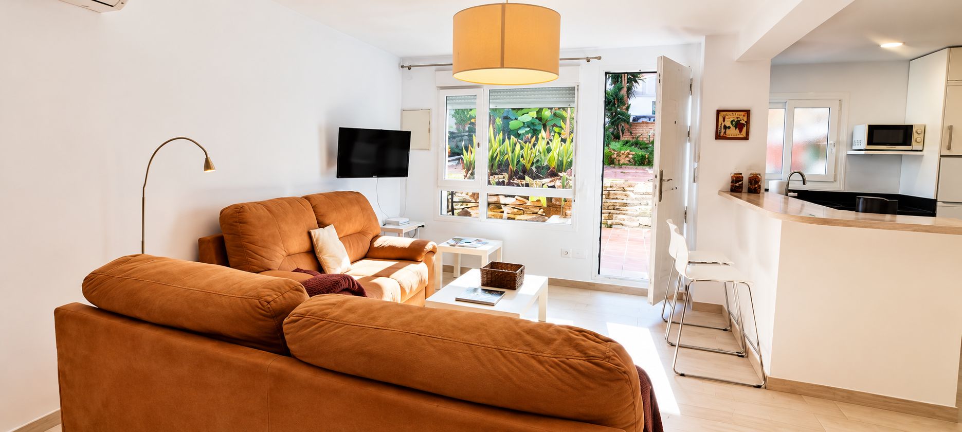 Ein modernes Wohnzimmer mit einer Couch, einem Fernseher und einem Fenster mit Blick auf Grünflächen.