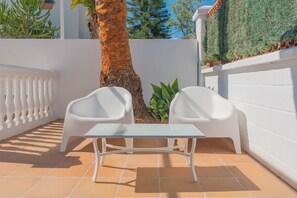 A white table with two white chairs on a tiled patio, surrounded by white walls and a palm tree. - Torremolinos Coliving Playa (Torremolinos)