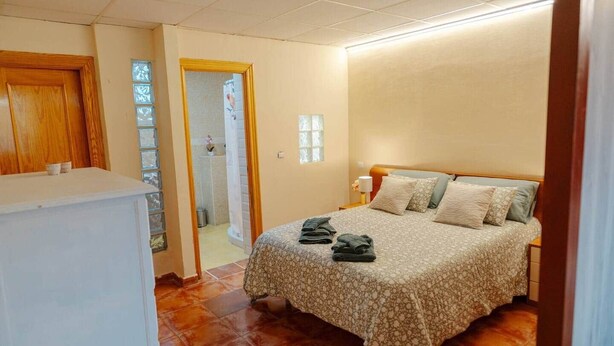 Un dormitorio con cama, armario de madera y baño visible a través de una puerta abierta.