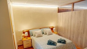 Un dormitorio con cabecera de madera, cama con colcha estampada, dos almohadas, una mesita de noche con lámpara y un panel de pared de madera.