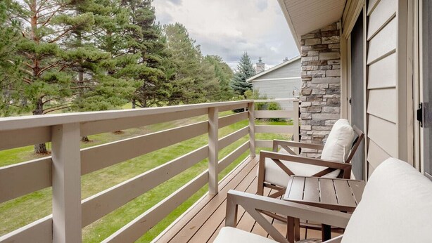 A wooden deck with a white railing, a stone wall, and a view of trees.