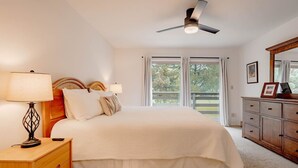 A bedroom with a bed, bedside tables, a ceiling fan, a dresser, and a window with a view of trees.