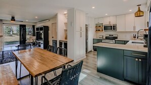 Cocina moderna con comedor, que incluye una mesa y sillas de madera, armarios blancos y una isla grande con un lavamanos.