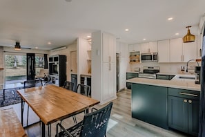 Eine moderne Küche mit Essbereich, ausgestattet mit einem Holztisch, Stühlen, weißen Schränken und einer großen Kochinsel mit Spüle.