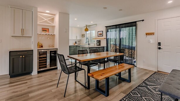 Una cocina moderna con armarios blancos, un comedor con mesa de madera y sillas negras, y una sala de estar con sofá gris.