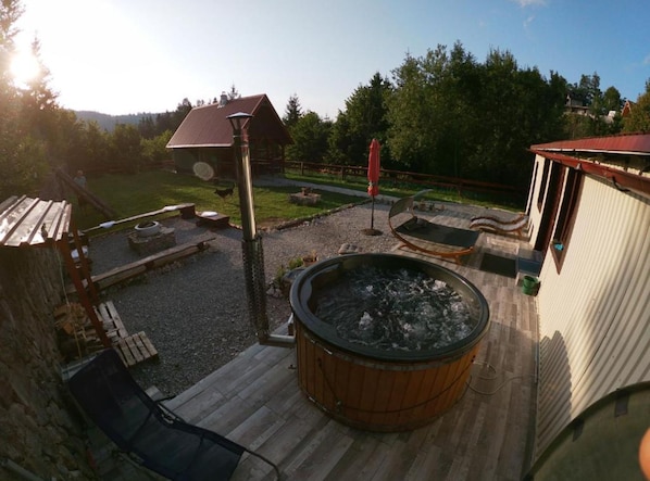 A wooden deck with a hot tub, outdoor seating, and a fenced yard.