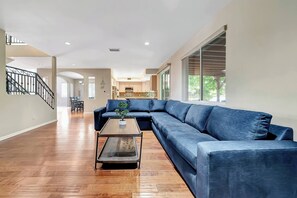 Ein geräumiges Wohnzimmer mit einem großen, blauen Ecksofa, einem Glastisch und einer Treppe, die zu einer weiteren Ebene führt.