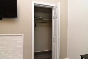 Ein Zimmer mit weißer Ziegelwand, einem flachbildfernseher über einer Tür und einem dunklen Holzboden.