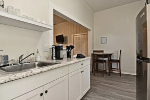 A kitchen with a granite countertop, stainless steel sink, and a dining area with a wooden table and chairs. - Studio Apt #3 in Historic Downtown Winter Garden, across from the Bike Trail (Winter Garden)