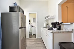 A kitchen with a stainless steel refrigerator, a countertop with a coffee maker, and a trash bin. - Studio Apt #3 in Historic Downtown Winter Garden, across from the Bike Trail (Winter Garden)