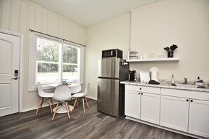 A modern kitchen with white cabinetry, a stainless steel refrigerator, a microwave, and a dining area with white chairs. - Chic Studio Apt #4 by Bike Trail & Historic Downtown Winter Garden (Winter Garden)