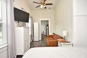 A bedroom with a bed, a ceiling fan, a TV, a dresser, a sofa, and a lamp. - Chic Studio Apt #4 by Bike Trail & Historic Downtown Winter Garden (Winter Garden)