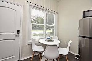 A kitchen with a white door, a round table with four chairs, a refrigerator, and a window with blinds. - Chic Studio Apt #4 by Bike Trail & Historic Downtown Winter Garden (Winter Garden)