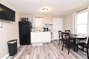 Eine kompakte Küche mit weißen Schränken, einem schwarzen Kühlschrank, einer Mikrowelle und einem Essbereich mit dunklen Holzsesseln und einem Tisch.