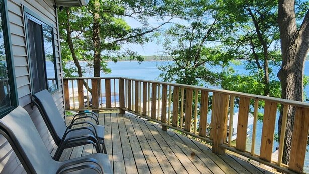 Een houten terras met stoelen, met uitzicht op water en bomen.