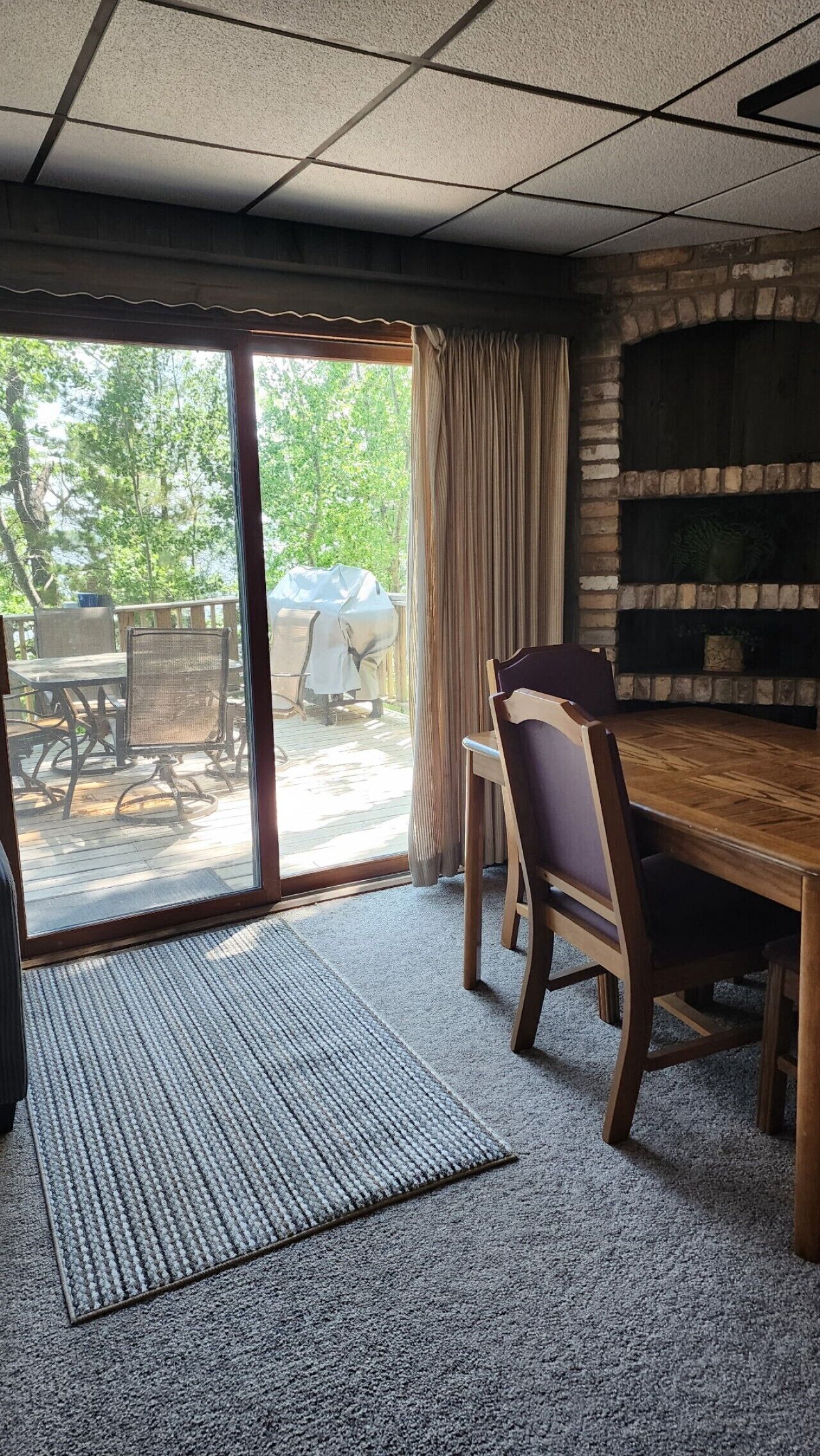A room with a fireplace, a dining table, chairs, a large window, and a view of the outdoors.