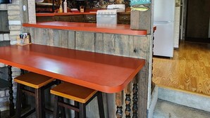 Een keuken met houten kastjes, een fornuis en een koelkast. Er is een bar met krukken en een houten tafel.