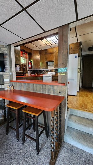 Une cuisine avec des meubles de rangement en bois, une cuisinière et un réfrigérateur. On y trouve également un coin bar avec des tabourets et une table en bois.