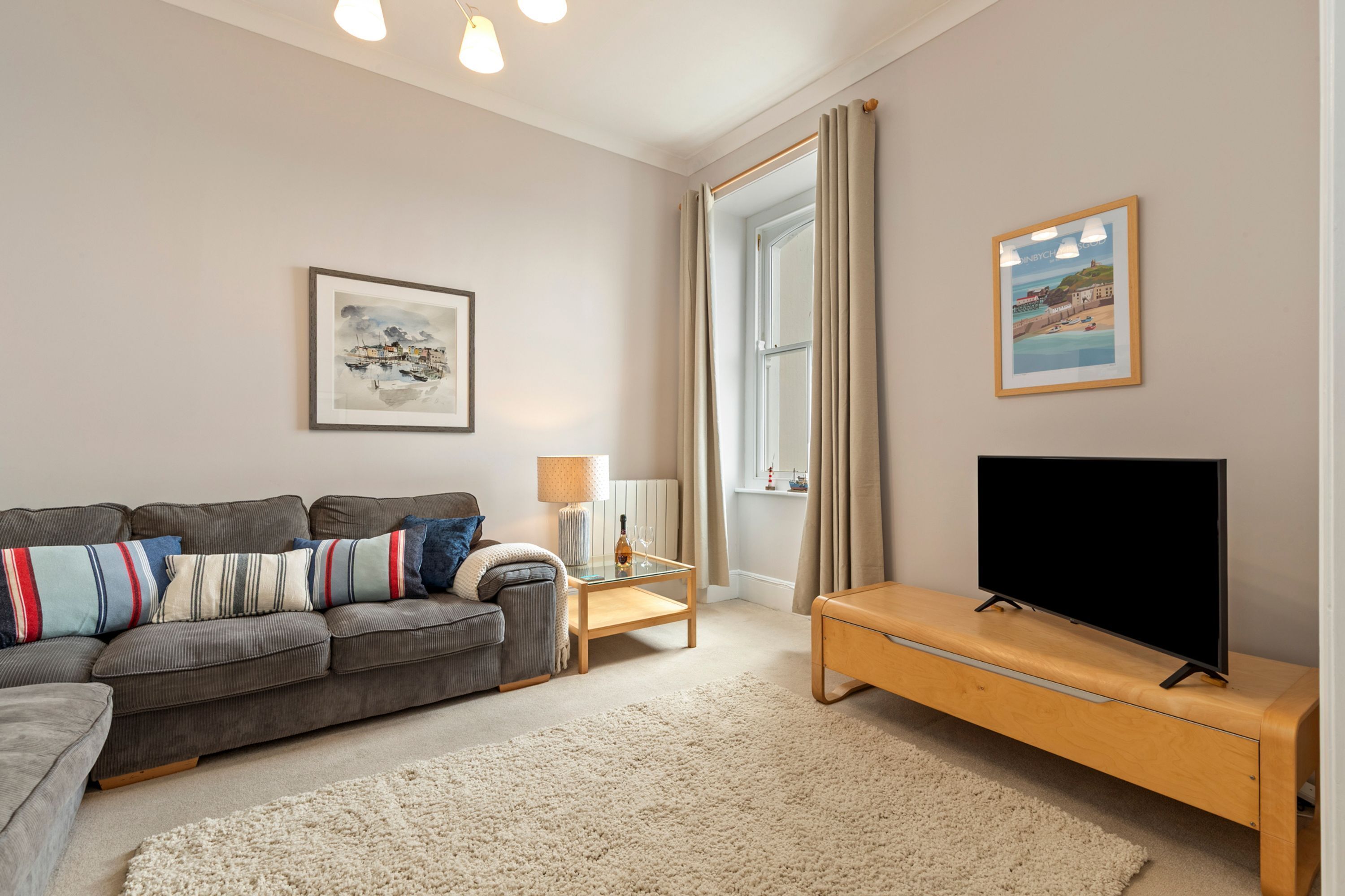 Een woonkamer met een bank, tv-meubel en een raam met gordijnen.