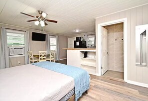 Ein Zimmer mit Bett, Schreibtisch, Stuhl, einer Küchenzeile und einem Deckenventilator.