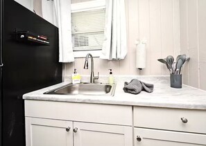 Eine Küche mit Spüle, einem Fenster mit Jalousien, einem Handtuchhalter und einer Besteckhalterung.