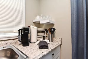 A kitchen with a coffee maker, stacked plates, a knife block, and a window with blinds. - Efficiency Apt #6 Near Downtown & Bike Trail (Winter Garden)