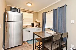 A compact kitchen with a refrigerator, microwave, and sink. There is a dining table with chairs and a window with curtains. - Efficiency Apt #6 Near Downtown & Bike Trail (Winter Garden)
