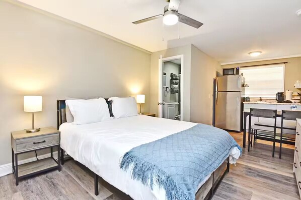 A bedroom with a bed, bedside tables, a ceiling fan, and a kitchenette with a refrigerator and microwave. - Efficiency Apt #6 Near Downtown & Bike Trail (Winter Garden)