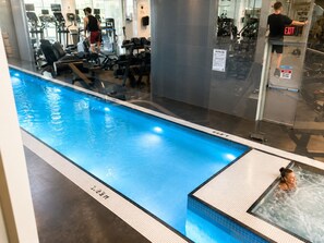 Ein Pool mit Whirlpool, Fitnessgeräten und einer Glaswand.