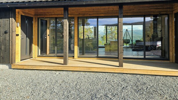 A modern building with large glass windows, wooden exterior, and a gravel ground.