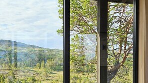 A view through large windows of a landscape with trees and hills.