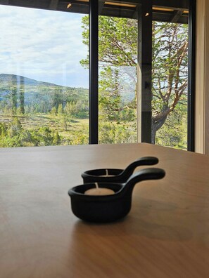 A view through large windows of a landscape with trees and hills.