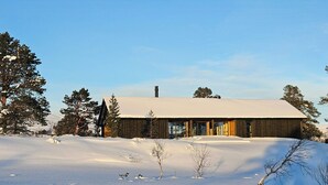 A wooden cabin with a snow-covered roof, surrounded by trees and a snowy landscape.