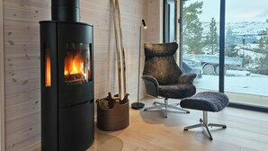 A modern interior with a wood-burning stove, a plush chair, and a large window offering a view of a snowy landscape.