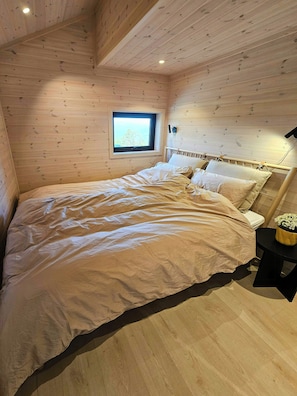 Un dormitorio con paneles de madera, una cama, una mesita de noche, un ventanal y una pequeña mesa con un florero.