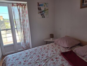 Une chambre Ă coucher avec un lit, une petite table, une lampe et une fenĂȘtre avec des rideaux.