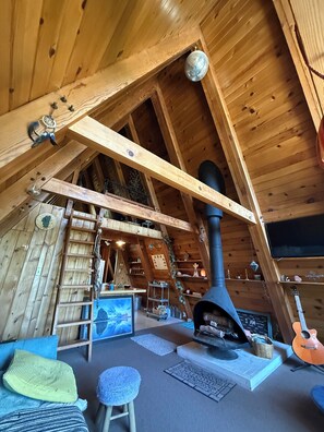 Ein gemütliches Dachzimmer mit Holzbalkendecke, Kamin, einer Wendeltreppe und einer kleinen Sitzecke mit Kissen.