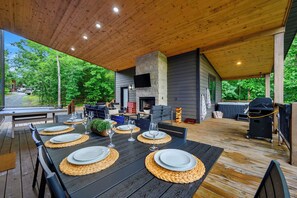Ein Essbereich im Freien mit Holzterrasse, Kamin aus Stein und Grill.