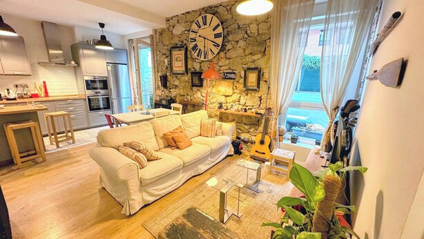 A living room with a sofa, a coffee table, a guitar, and a stone wall with a clock. - Pepe house (Areeta / Las Arenas)