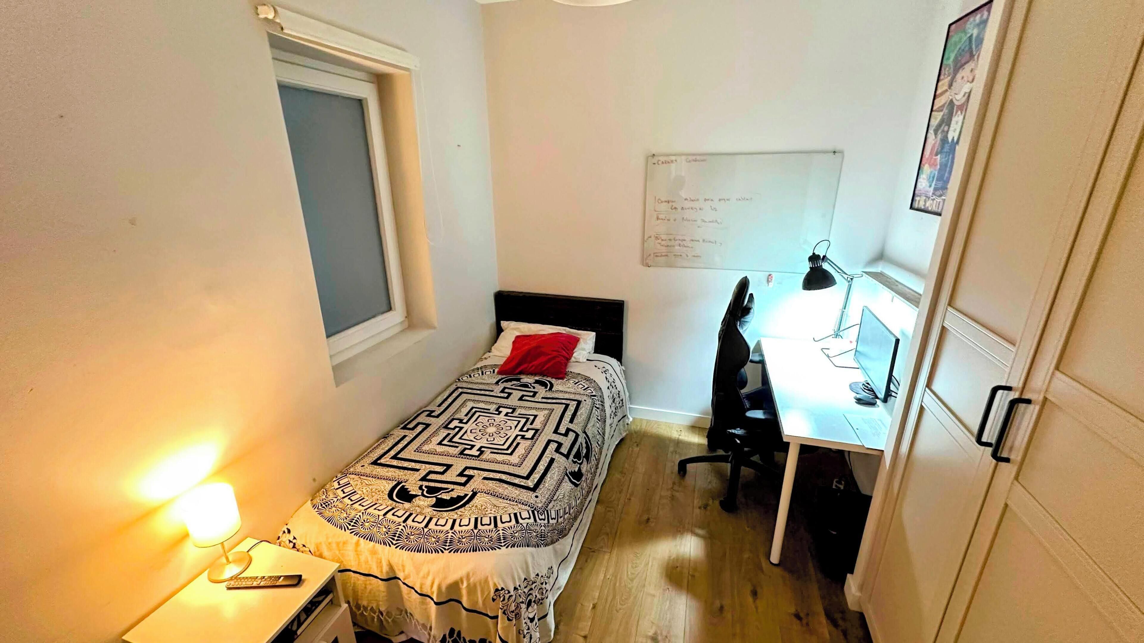 Una habitación pequeña con cama, escritorio, silla y una pizarra en la pared.