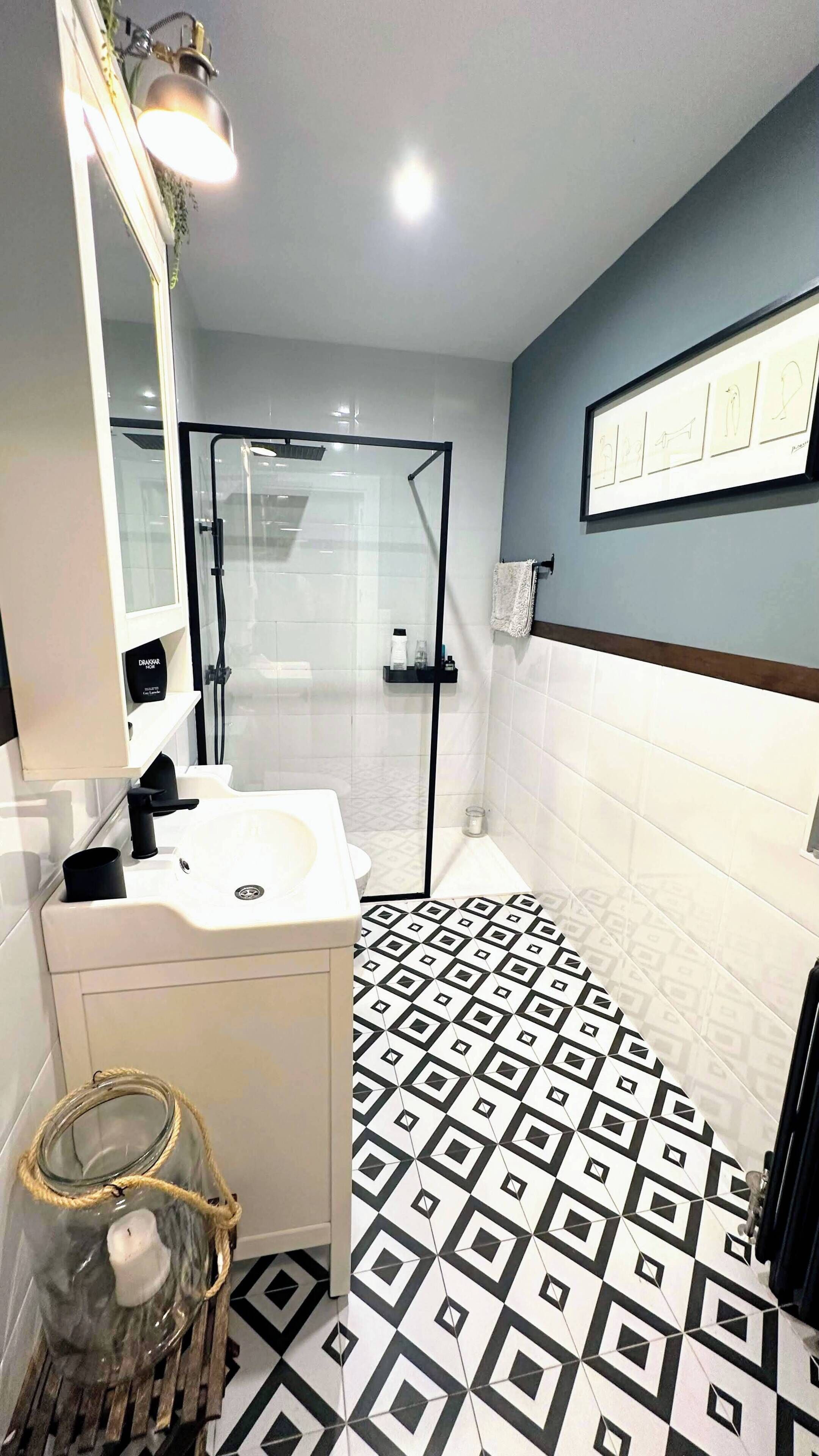 Un baño con cabina de ducha de vidrio, un lavabo con espejo y suelo estampado.